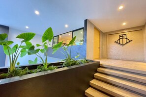 A modern interior with a staircase leading to a second floor, a concrete planter with greenery, and a wall-mounted logo.