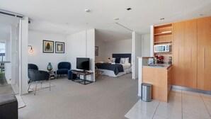 Ein modernes Hotelzimmer mit Bett, Schreibtisch, Stuhl, Fernseher und einer Küchenzeile.