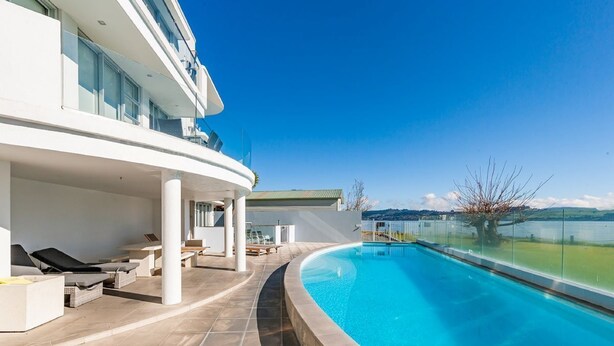 Ein modernes Hotel mit einem geschwungenen Pool, Sitzgelegenheiten im Freien und Seeblick.