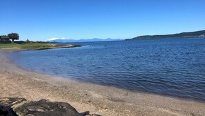 Ein Strand mit ruhigem Wasser, blauem Himmel und fernen Bergen.