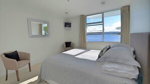 Une chambre avec un grand lit, une chaise, une télévision et une fenêtre donnant sur l’eau.