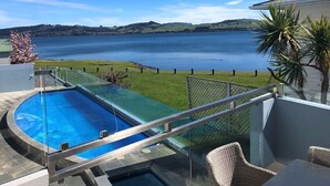 Une piscine dotée d’une paroi en verre, offrant une vue sur un lac bordé de collines.