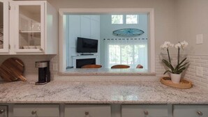 Una cocina con televisor integrado, cafetera y ventana con vista a una sala de estar.