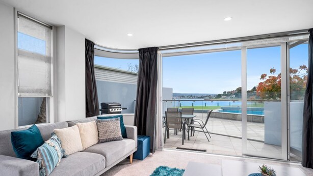 Una sala de estar moderna con un sofá gris, una mesa de centro y vistas a una piscina y vegetación.