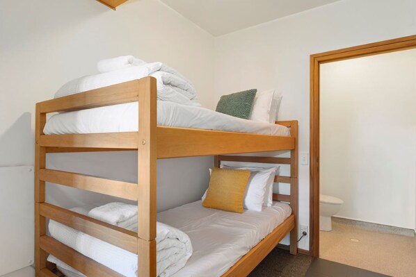 A bunk bed with white bedding and a yellow pillow.