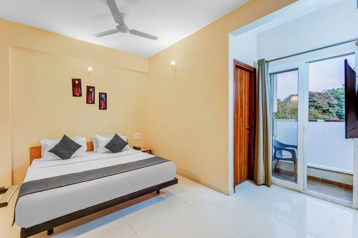 A modern hotel room with a large bed, ceiling fan, and a balcony with a view.