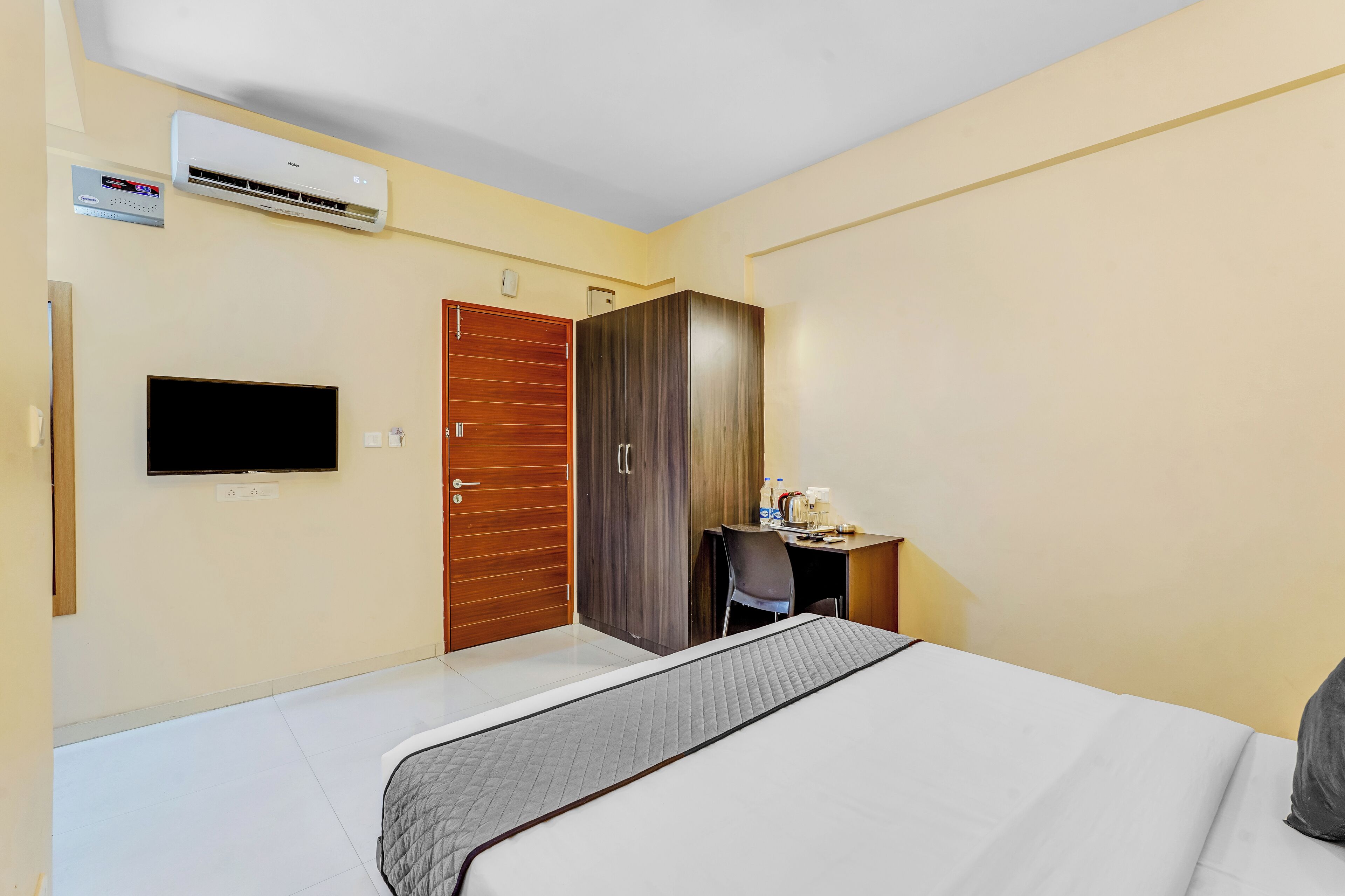 A hotel room with a bed, a desk, a chair, an air conditioning unit, a television, and a wardrobe.