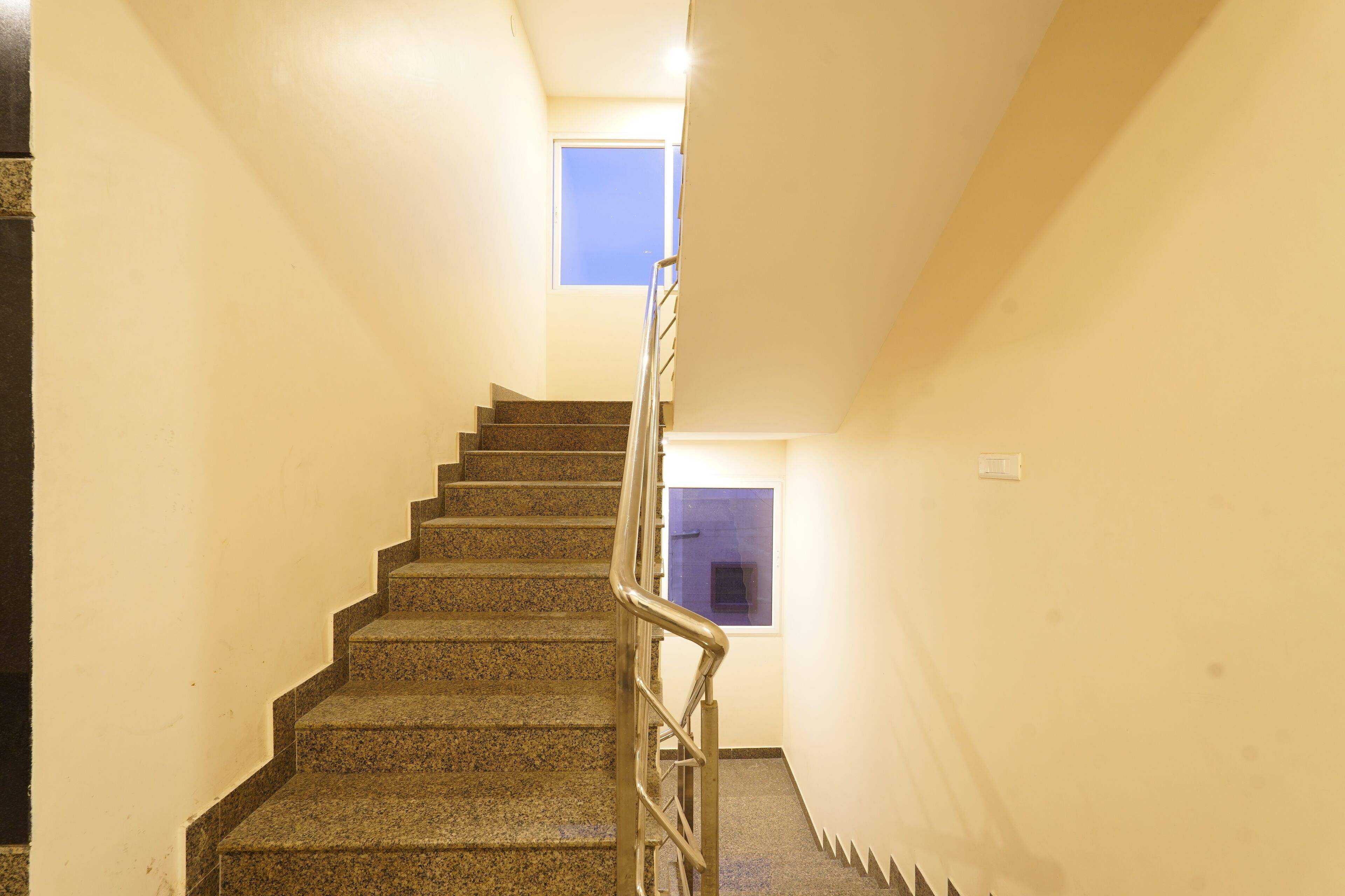 A staircase with a metal handrail leading to a landing with a small window.