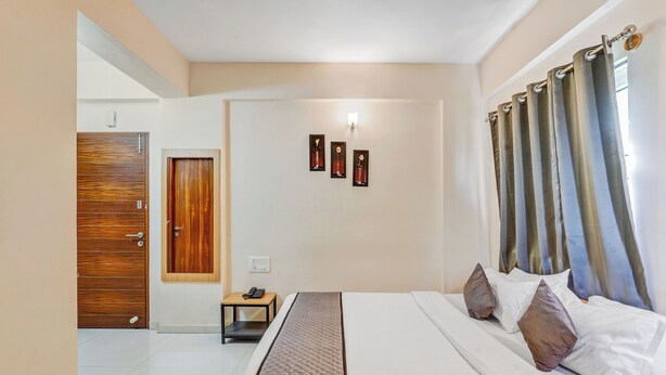 Una habitación de hotel con una cama, una mesita de noche, una puerta de madera y una lámpara fijada a la pared.