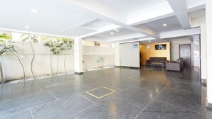 Un vestíbulo amplio con techo alto, suelo de baldosas y una zona de estar con sofá y sillones.