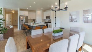A modern kitchen with white cabinets, a central island, and a dining area with a wooden table and chairs. - Red Rock Haven - NEW Private Pool, putting green, & more. Perfect family retreat (Washington)