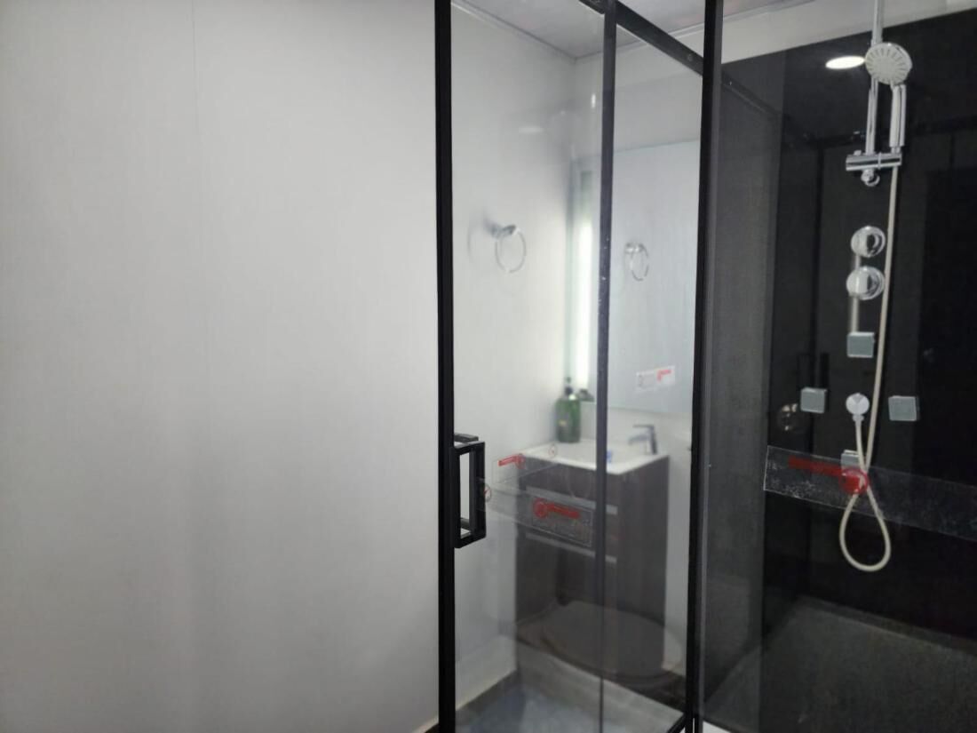Un baño moderno con cabina de ducha de vidrio, lavamanos visible y ducha de mano.