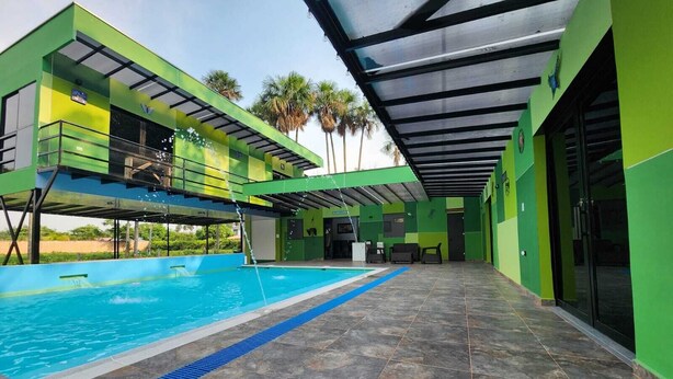 A modern pool area with a clear blue pool, green walls, and a covered seating area. - Encanto Llanero Xkpdestinations (Villavicencio)