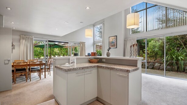 Una cocina moderna con una isla central, ventanas amplias y un comedor con vistas a zonas verdes.