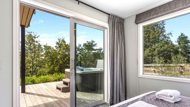 Een slaapkamer met een grote schuifglazen deur die uitkomt op een terras, een jacuzzi en uitzicht op bomen.