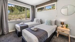 Een hotelkamer met twee bedden, een klein nachtkastje met een lamp, een spiegel en uitzicht op groen.