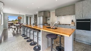 Een moderne keuken met een lang houten kookeiland, barstoelen en uitzicht op de omgeving.