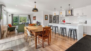 Une cuisine moderne avec des meubles blancs, un îlot central doté de tabourets et un coin repas avec une table et des chaises en bois.