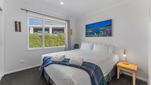 Une chambre d’hôtel avec un grand lit, une table de chevet avec une lampe, un tableau représentant un paysage urbain et une fenêtre donnant sur un espace verdoyant.
