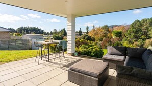 Une terrasse extérieure avec une table et des chaises, un coin salon confortable et une vue sur un quartier résidentiel.