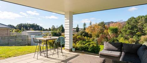 An outdoor patio with a table and chairs, a cushioned seating area, and a view of a residential neighborhood.