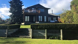 A modern two-story house with a balcony, a large tree in the front yard, and a well-maintained lawn.
