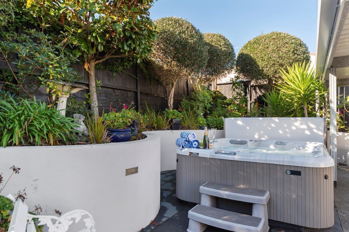 Una vasca idromassaggio con gradini, immersa in un giardino con diverse piante e un muro bianco.