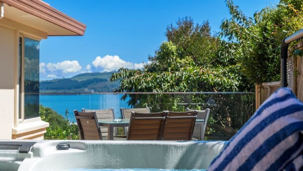 A hot tub with a view of a lake and mountains, surrounded by wooden chairs and a table. - Tui Lookout Hot Tub and Views (Taupo)
