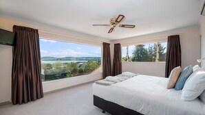 A bedroom with a large bed, a ceiling fan, and a view of a landscape through large windows. - Tui Lookout Hot Tub and Views (Taupo)