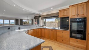 A modern kitchen with granite countertops, wooden cabinets, and a large built-in oven. - Tui Lookout Hot Tub and Views (Taupo)
