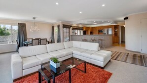 A modern living room with a sectional sofa, a glass coffee table, and a red rug. - Tui Lookout Hot Tub and Views (Taupo)