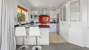 A modern kitchen with white cabinets, a red accent wall, and a central island with two bar stools. - Top of the Lake in Taupo (Taupo)