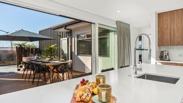 A modern kitchen with a white countertop, a dining area with a wooden table and chairs, and a view of the outdoors. - Nga Roto Retreat with Hot Tub (Taupo)