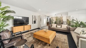 A modern living room with a flat-screen TV, a sofa, a coffee table, and a large plant. - Nga Roto Retreat with Hot Tub (Taupo)