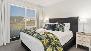 A hotel room with a large bed, a nightstand, and a view of a road and greenery outside. - Nga Roto Retreat with Hot Tub (Taupo)