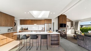 A modern kitchen with a central island, bar stools, and a dining area with a sofa and coffee table. - Nga Roto Retreat with Hot Tub (Taupo)