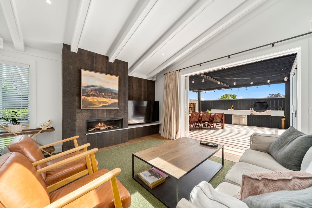 Una sala de estar moderna con chimenea, televisor y comedor, con una cocina al fondo.
