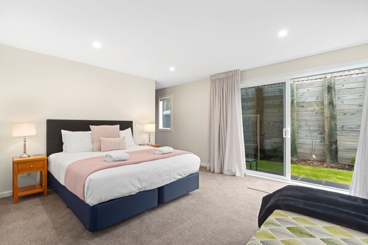 A bedroom with a bed, nightstands, a window, and a sliding glass door leading to a garden.