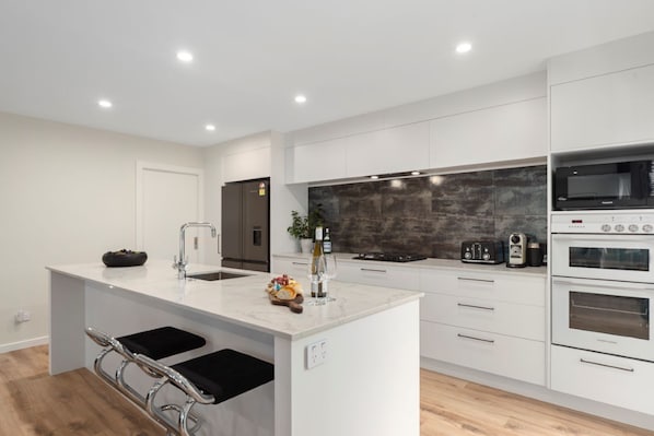 A modern kitchen with white cabinetry, a marble island, stainless steel appliances, and a black backsplash. - Sanctuary on the Grove Taupo (Taupo)