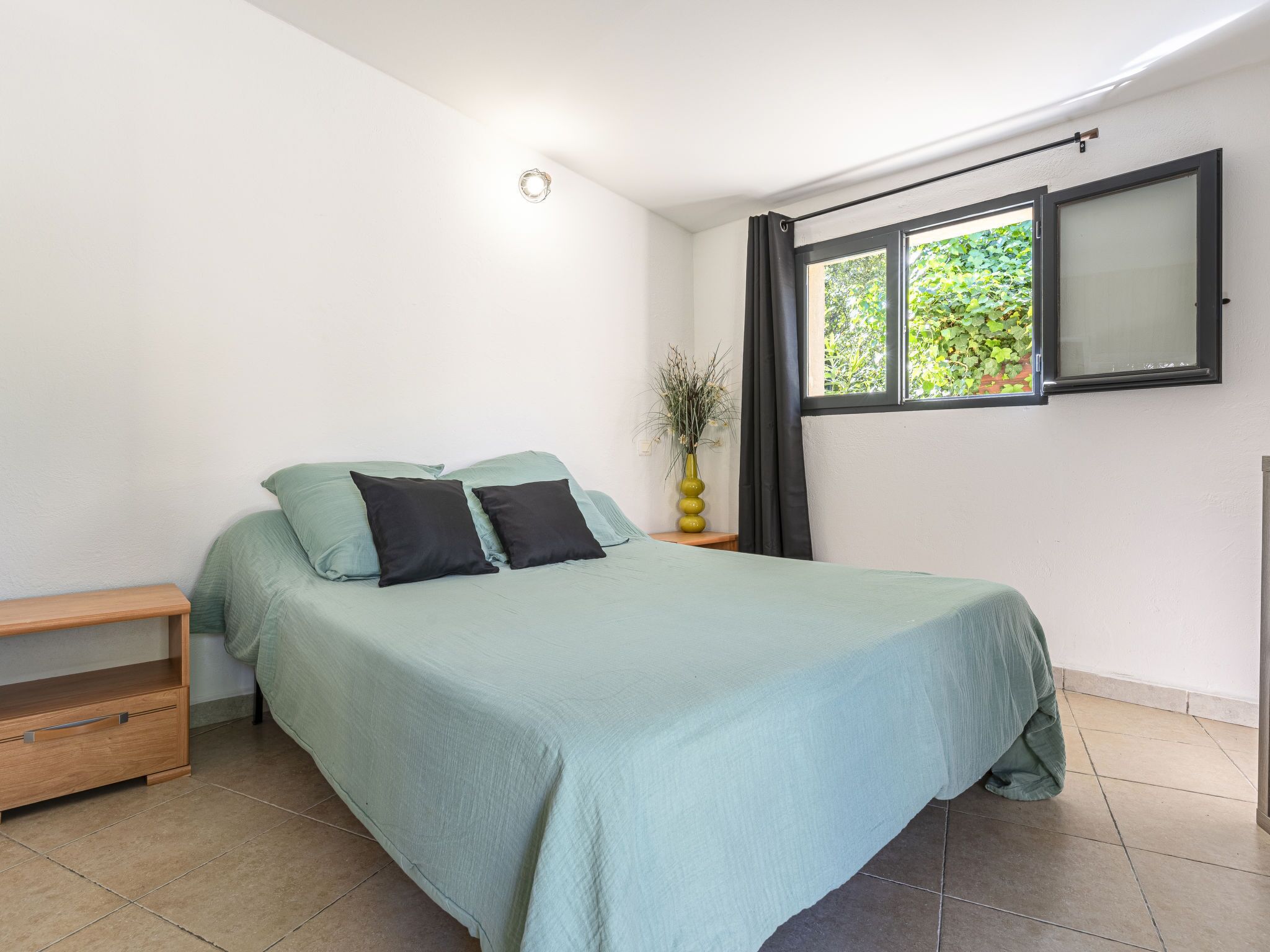 Une chambre à coucher comprenant un lit, une table de chevet, une commode, une fenêtre avec des rideaux et un téléviseur fixé au mur.