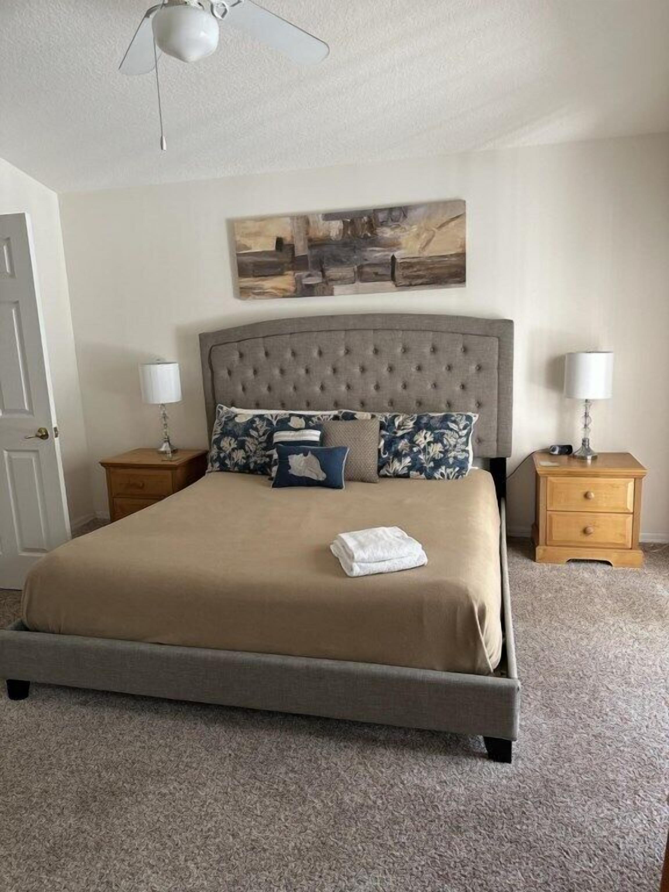 A neatly arranged bedroom with a large bed, two bedside tables, and a ceiling fan.