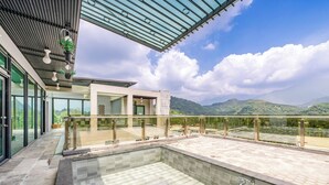 A modern outdoor pool area with a glass balustrade, a stone-tiled floor, and a view of the surrounding landscape. - Han Yan Hill Hotel (Yuchi)