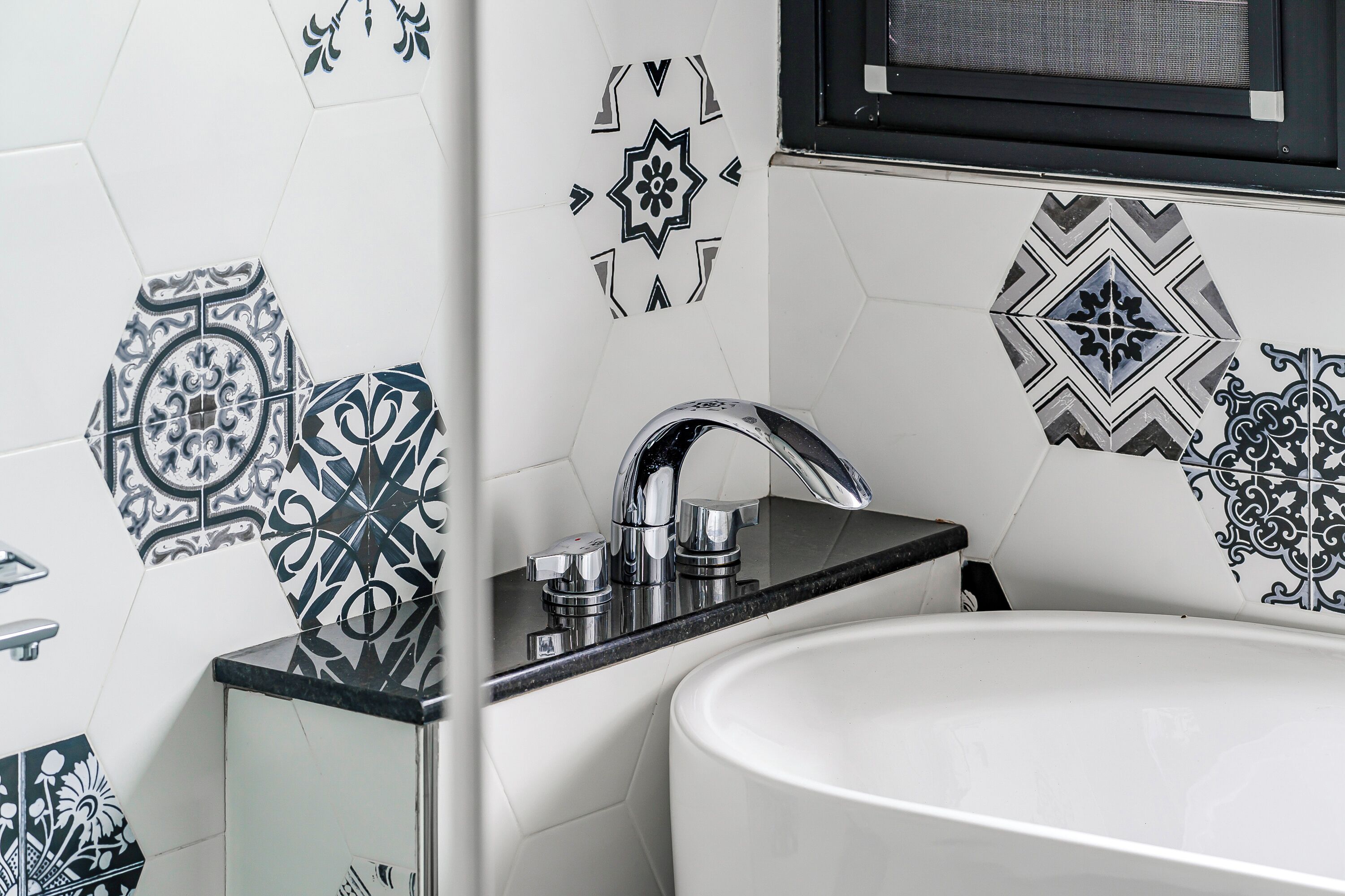 Une salle de bain avec un lavabo blanc, un plan de toilette noir et des carreaux décoratifs noirs et blancs sur les murs.