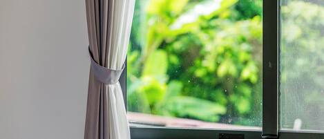 A window with a curtain tied at the top, a view of greenery outside, and a window screen.