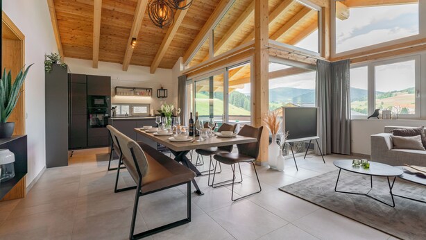 A modern interior with a dining area, kitchen, and living space with large windows offering scenic views.