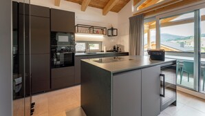 A modern kitchen with a central island, built-in appliances, and a large window offering a view of the countryside.