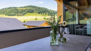 A table with a vase of flowers and wine glasses on a balcony overlooking a green landscape.