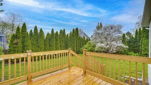 Eine Holzterrasse mit Geländer, umgeben von einem gepflegten Rasen und hohen Bäumen.
