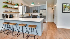 A modern kitchen with a central island, bar stools, and built-in appliances. - Swanton Retreat w/ Game Room, Hot Tub & Trails! (Swanton)