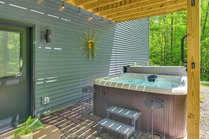 A modern outdoor hot tub area with a wooden deck, a metal chair, and a potted plant.